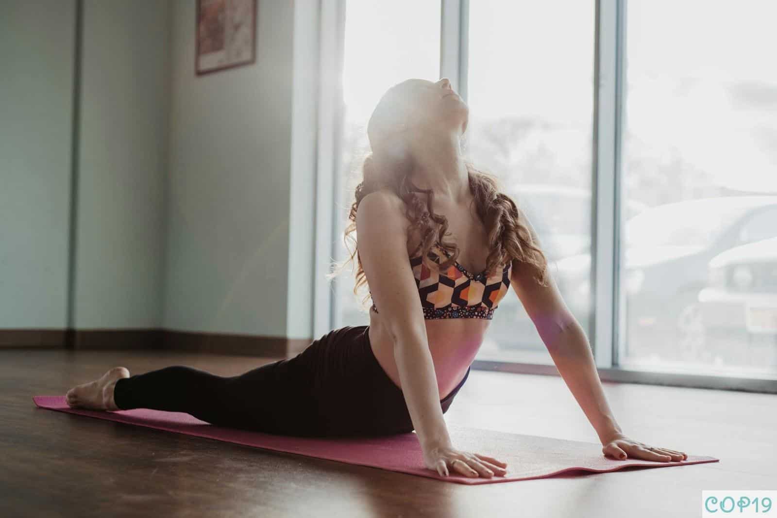 woman in black and white floral brassiere and black pants kneeling on pink yoga mat